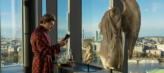 Andy Serkis as a cyber-killer reading a book in front of statues in Luther: Fallen Sun.